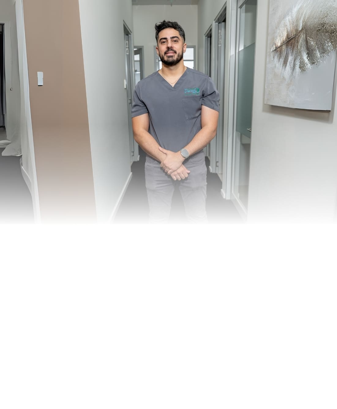 Professional male dental staff member in grey scrubs standing in a clinical hallway at Dandenong Dental Care clinic.