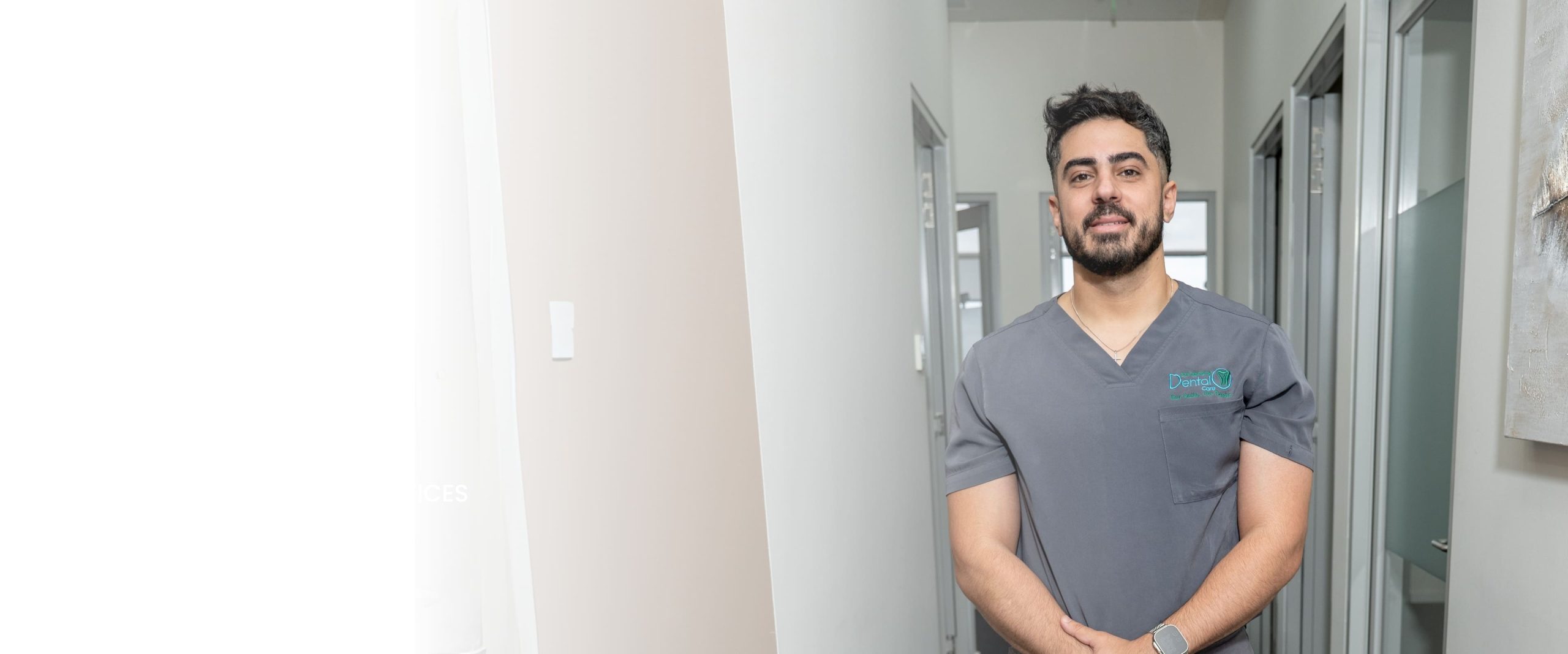 Professional male dental staff member in grey scrubs standing in a clinical hallway at Dandenong Dental Care clinic.
