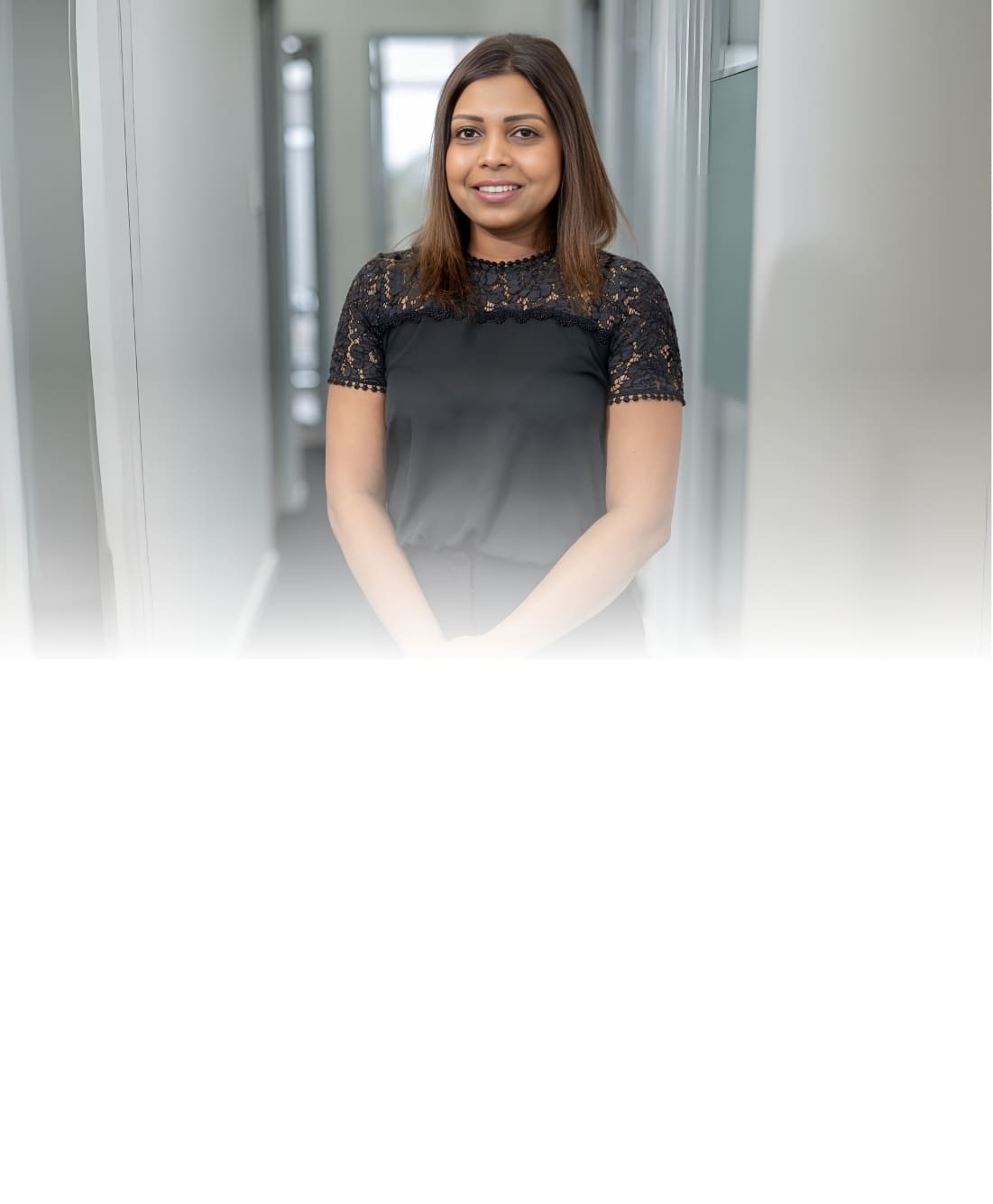 Female staff member with brown hair wearing a black lace top smiling in a bright clinic hallway at Dandenong Dental Care.